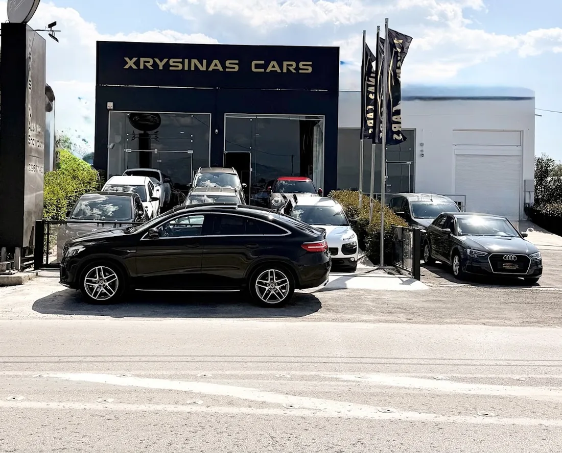 Η πρόσοψη της έκθεσης Xrysinas CARS: μαύρο κτίριο με χρυσή επιγραφή και αυτοκίνητα μπροστά